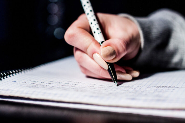 hand holding a pen and writing in a notebook